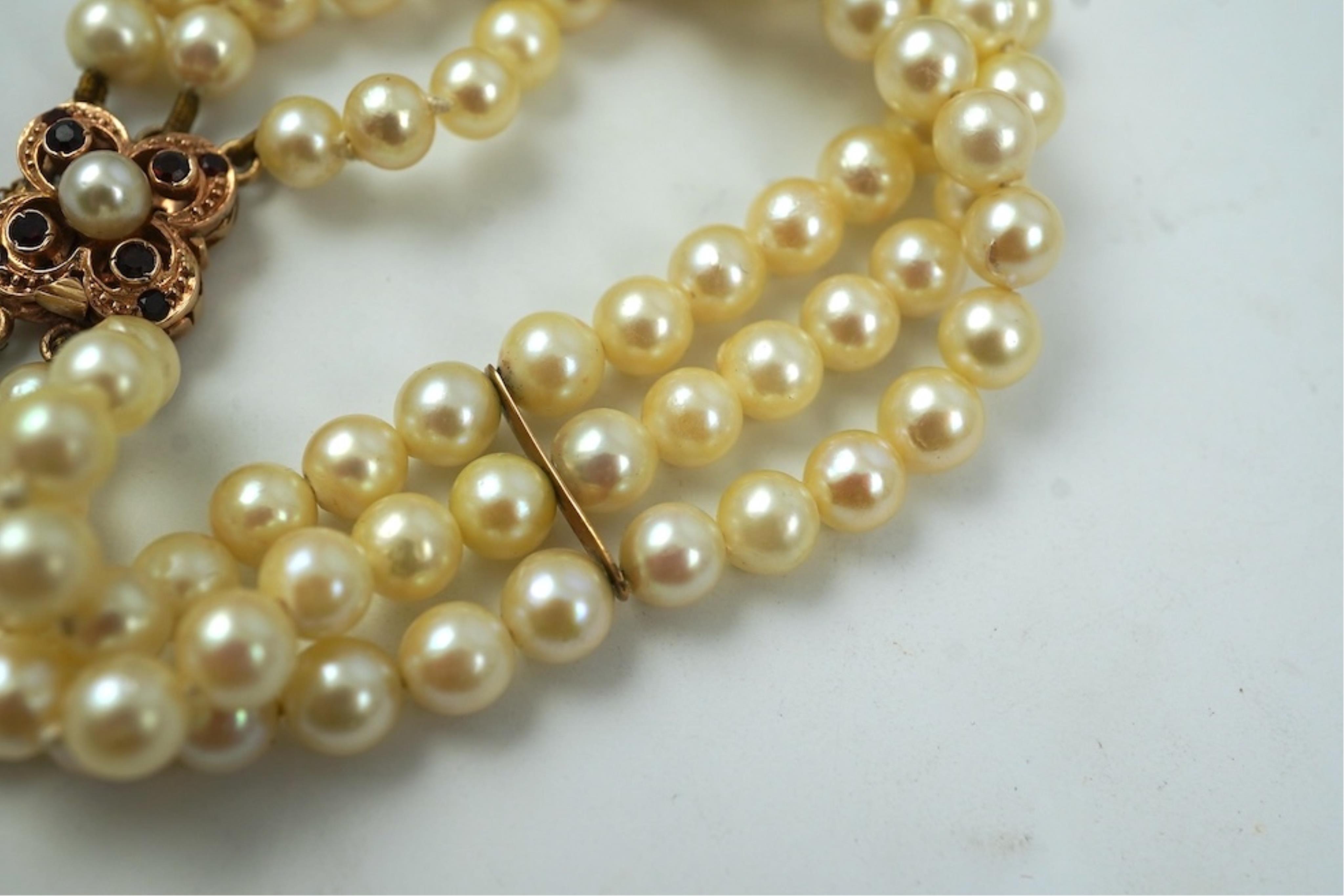 A triple strand cultured pearl bracelet, with a 9ct gold, garnet and cultured pearl cluster set clasp, 16cm.